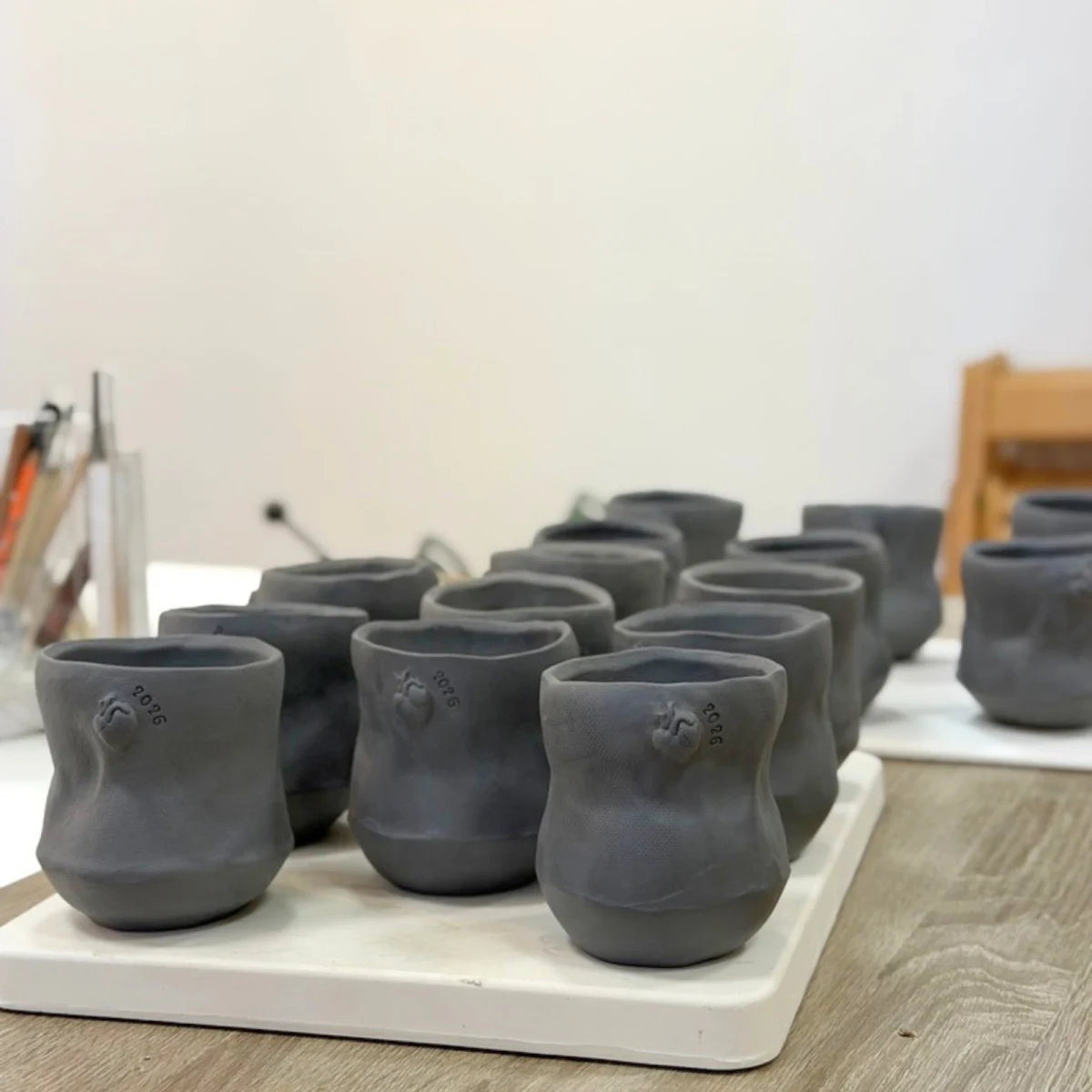 Handmade mugs from a custom order, each with a small anatomical heart, drying unfired in the studio